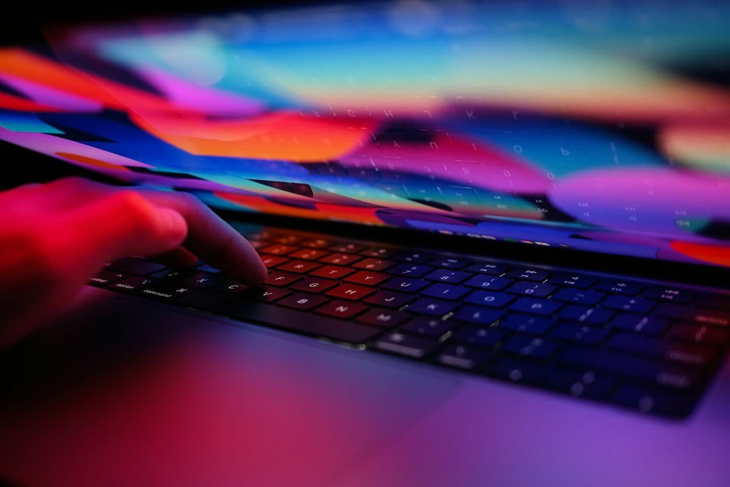 Ruky píšuce na klávesnici notebooku s abstraktnou digitálnou grafikou.